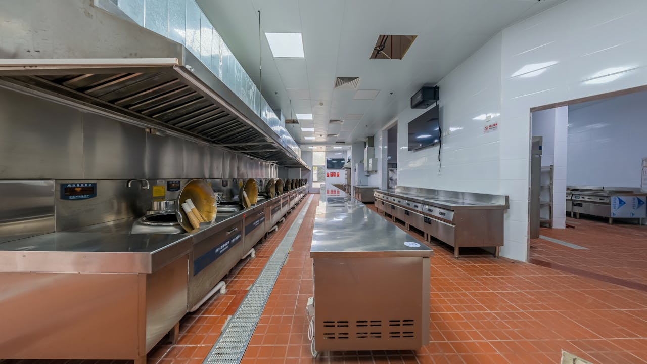 services-04 Modern industrial kitchen interior featuring stainless steel appliances and tiled flooring, ideal for commercial use.